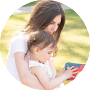 Mother and young child sitting outdoors on grass, focused on a colorful book together.